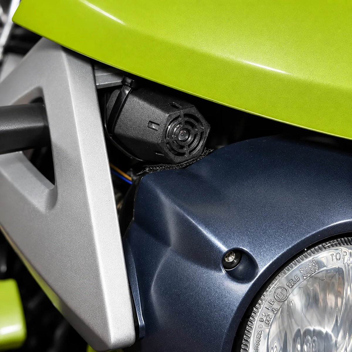 Frontpartie eines grünen Motorrads mit Scheinwerfer, an der Gabelbrücke sitzt ein schwarzes Bauteil